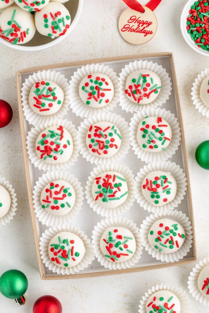 A box made of white chocolate with cookies, each in a cupcake lining, topped with red and green sprinkles. 