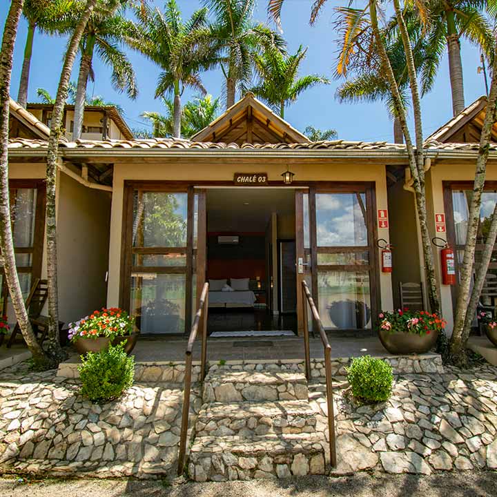 Imagem de uma cabana aconchegante de praia com entrada de vidro, cercada por palmeiras e flores coloridas, ideal para férias em resort tropical.