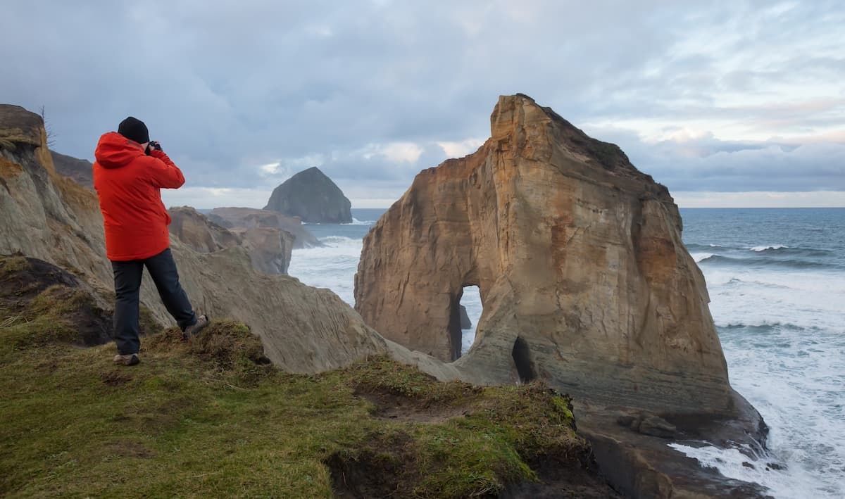 Hiker in red jacket taking a picture of Haystack Rock at Cape Kiwanda near Pacific City