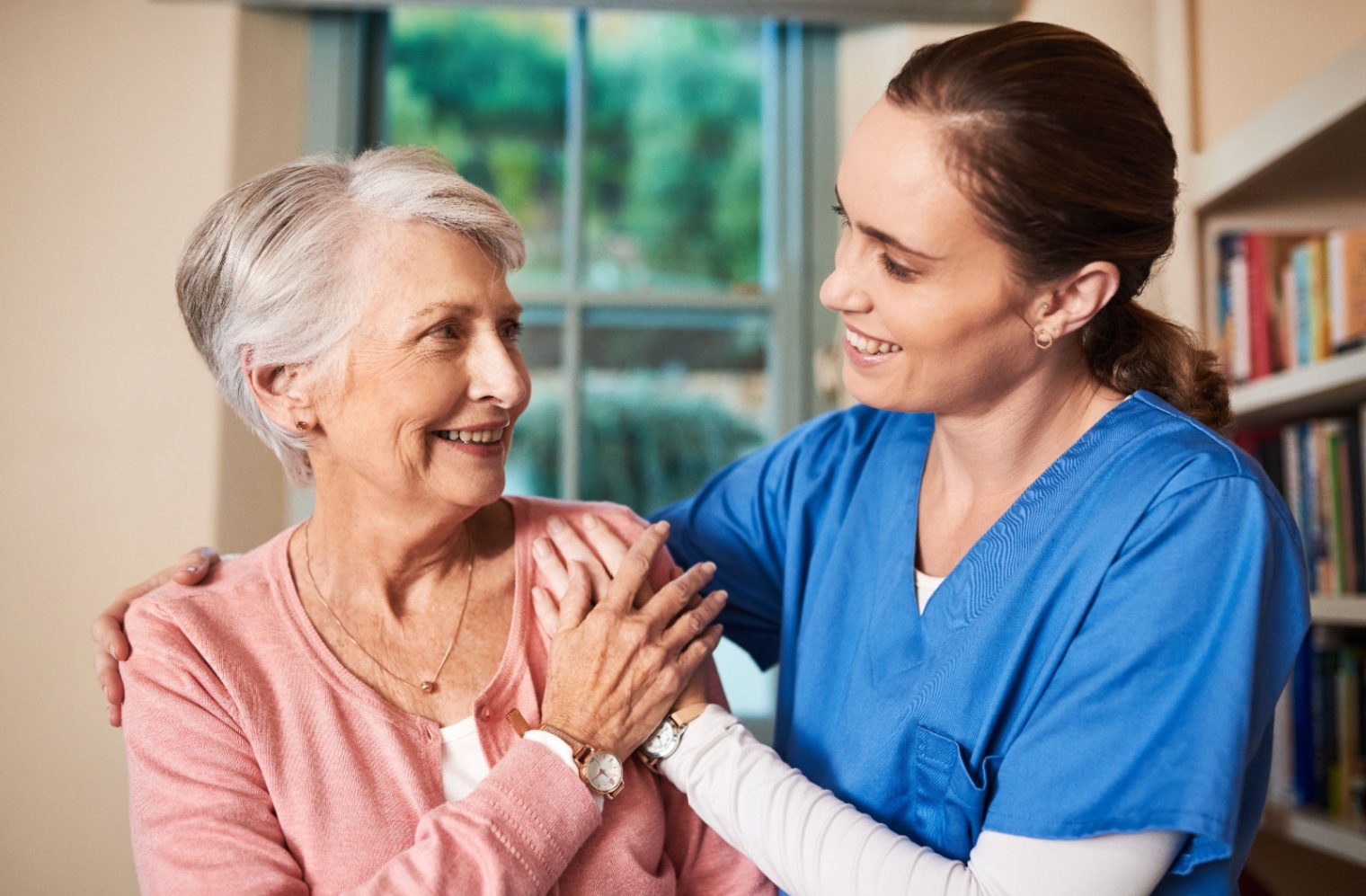 A caregiver with her arms around a smiling senior woman supporting her emotionally in memory care.