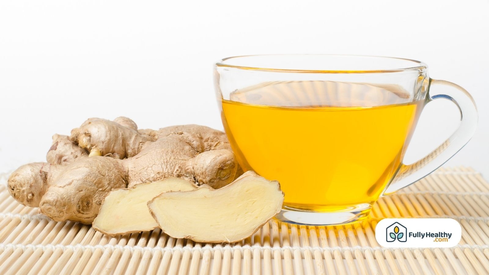 Clear cup of ginger tea beside raw sliced ginger root