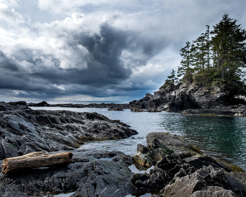 Dark sky reflecting on water with rocks along the shoreline.