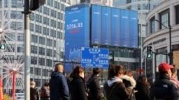 2025年1月21日， 上海街道上等候交通信号灯的行人与街头电子广告牌上显示的沪深股票指数。