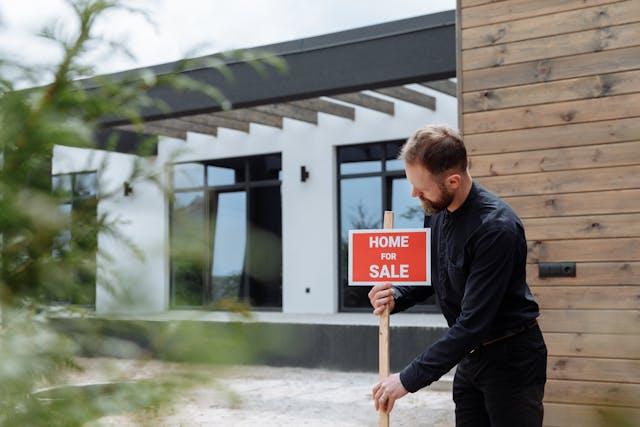 A man standing next to a red sign in front of a large house