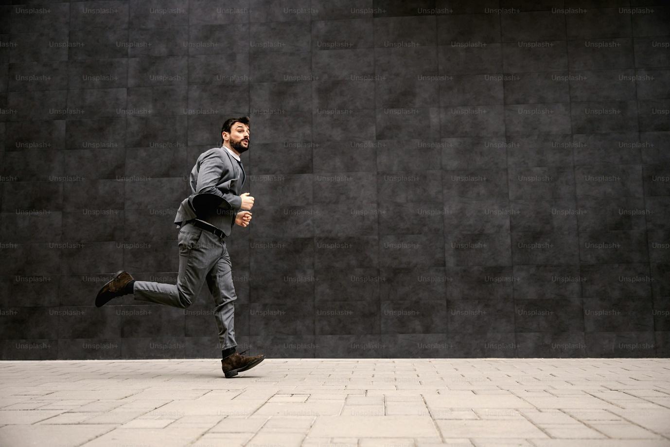 Young fashionable businessman running on the street. He is late for work.