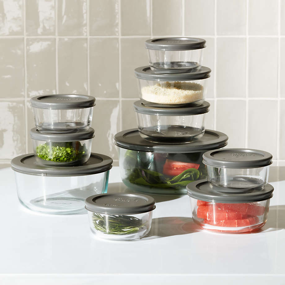 An assortment of glass, non-toxic Tupperware containers with food on a white countertop with a beige tile backsplash