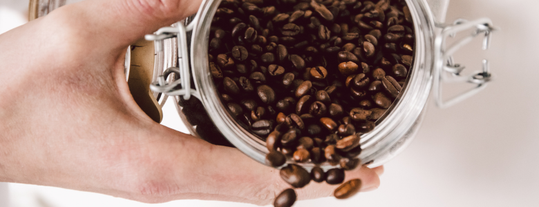 A hand holding organic coffee beans in an airtight jar