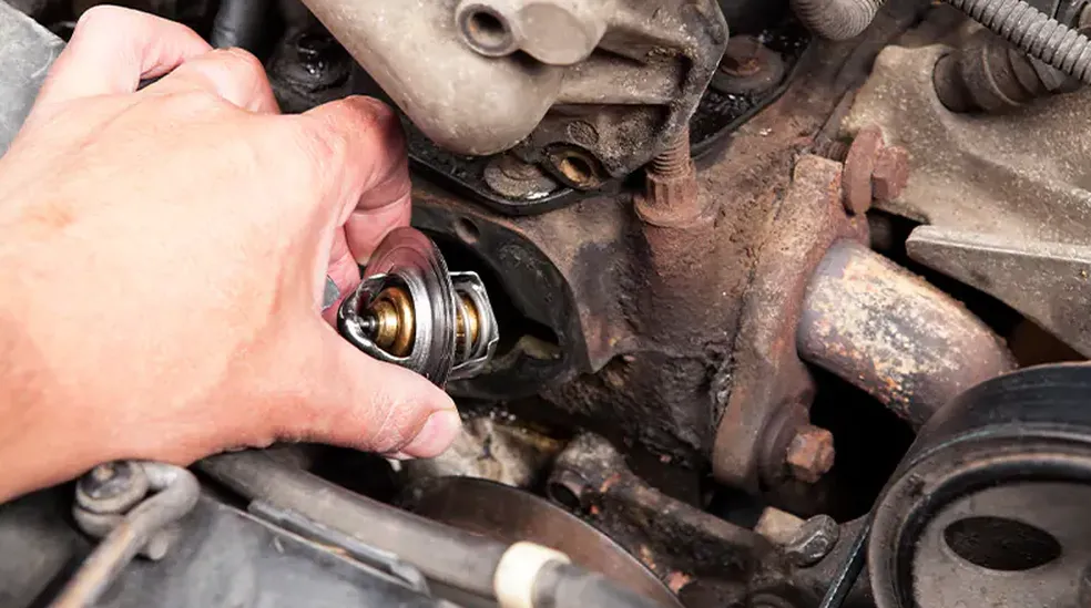 Mão masculina desroscando uma válvula termostática na parte interna do carro.