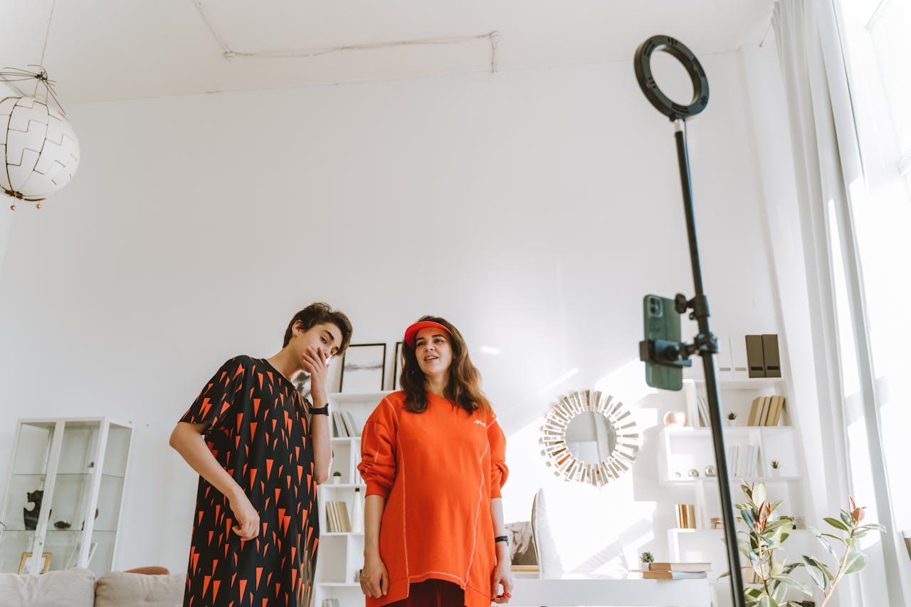 Two content creators filming in a bright room, with a ring light and phone set up in front of them, ready to create AI music for their video.