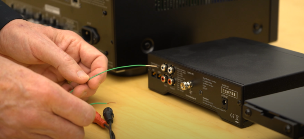 Person connecting a ground wire to the back of an audio receiver with multiple RCA inputs.