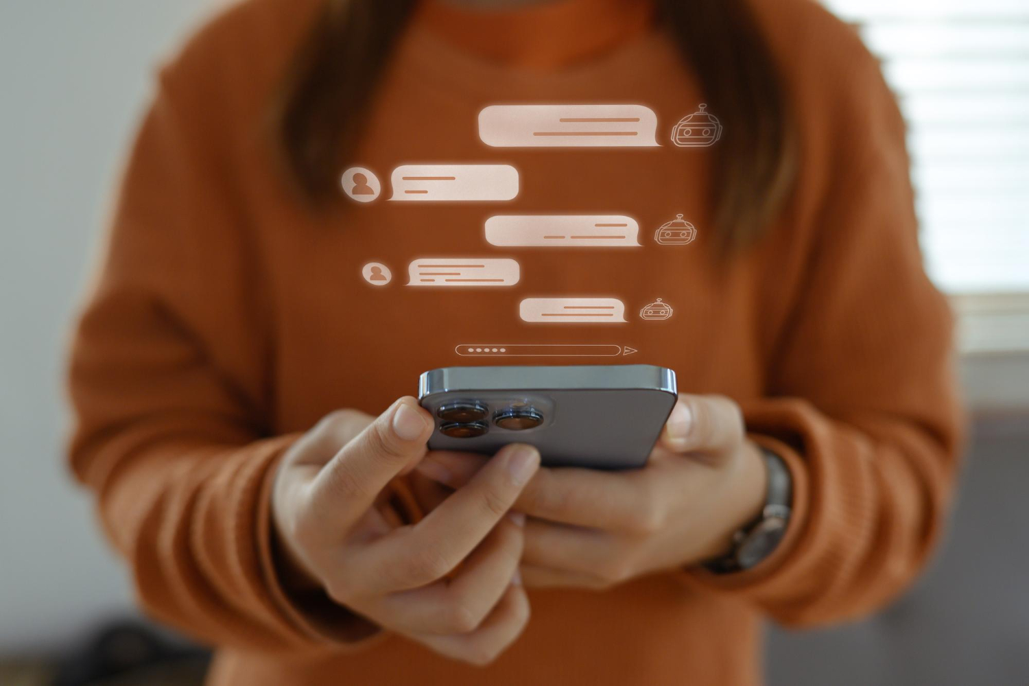 A imagem mostra uma pessoa segurando um smartphone, com mensagens flutuando acima do dispositivo. Essas mensagens representam uma mensagem automática para clientes, sugerindo uma interação virtual e eficiente. A pessoa está vestindo um suéter laranja, e o ambiente ao fundo é iluminado, com luz natural entrando pela janela.