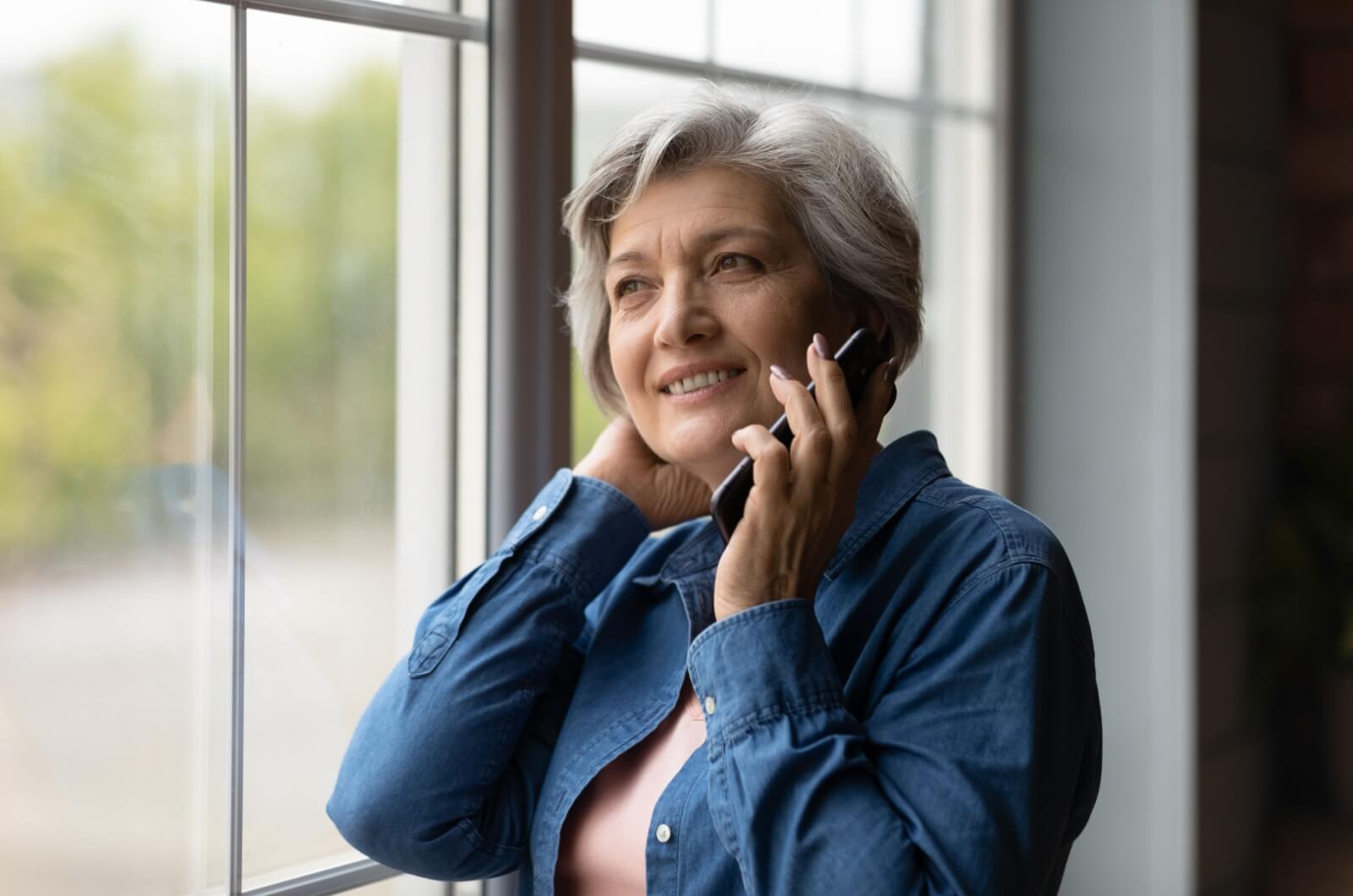 A smiling parent in assisted living talking to their adult child on the phone.