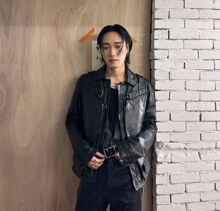 This contain DPR Artic standing in front of a wall wearing a leather jacket and black pants