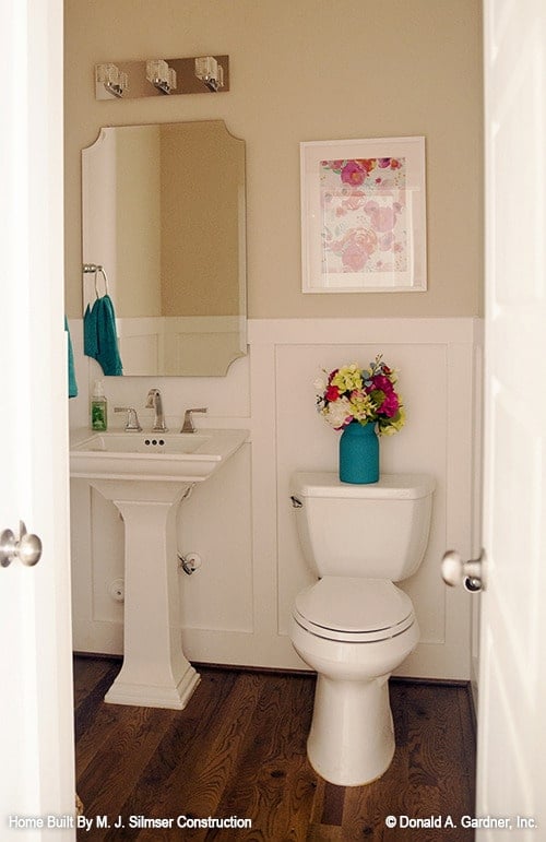 Powder room with wainscoted walls, a toilet, and a sink pedestal paired with a frameless mirror.