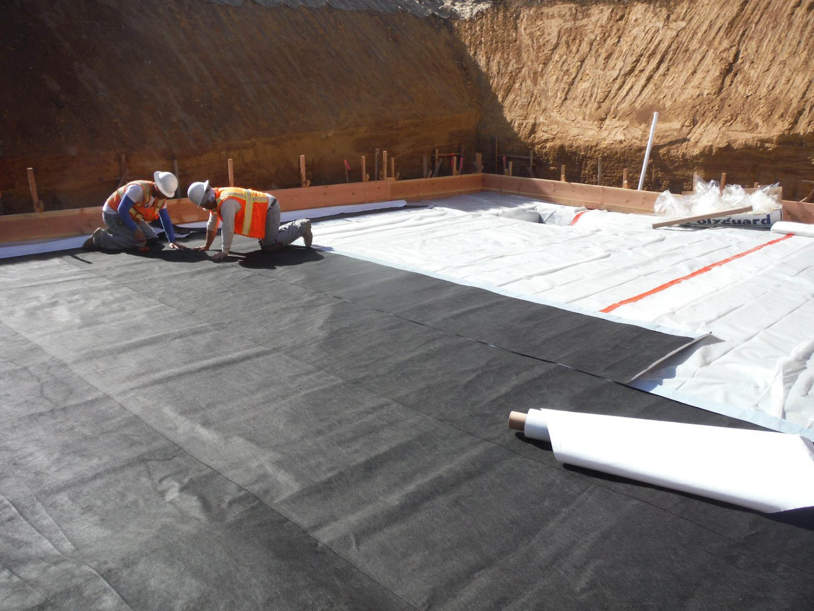 Workers complete garage floor waterproofing by applying a moisture barrier in a new home.