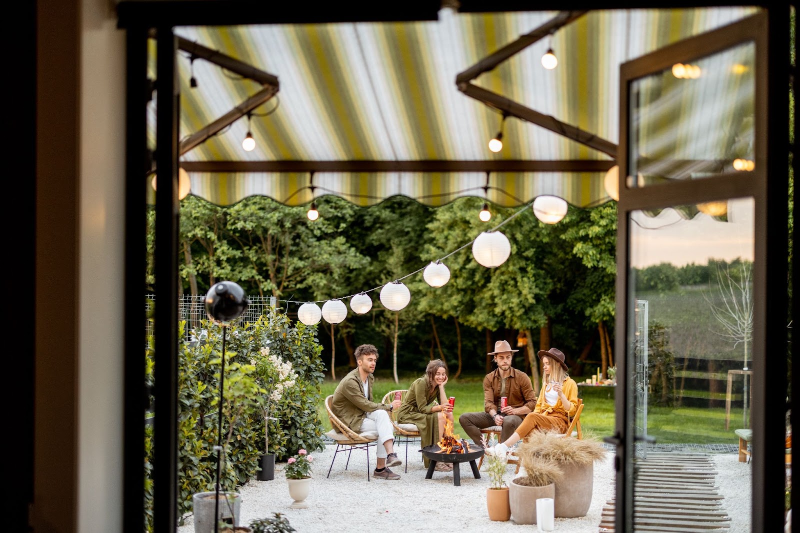 Friends gathered by an outdoor fireplace with striped awnings covering the patio door entrance in the foreground.