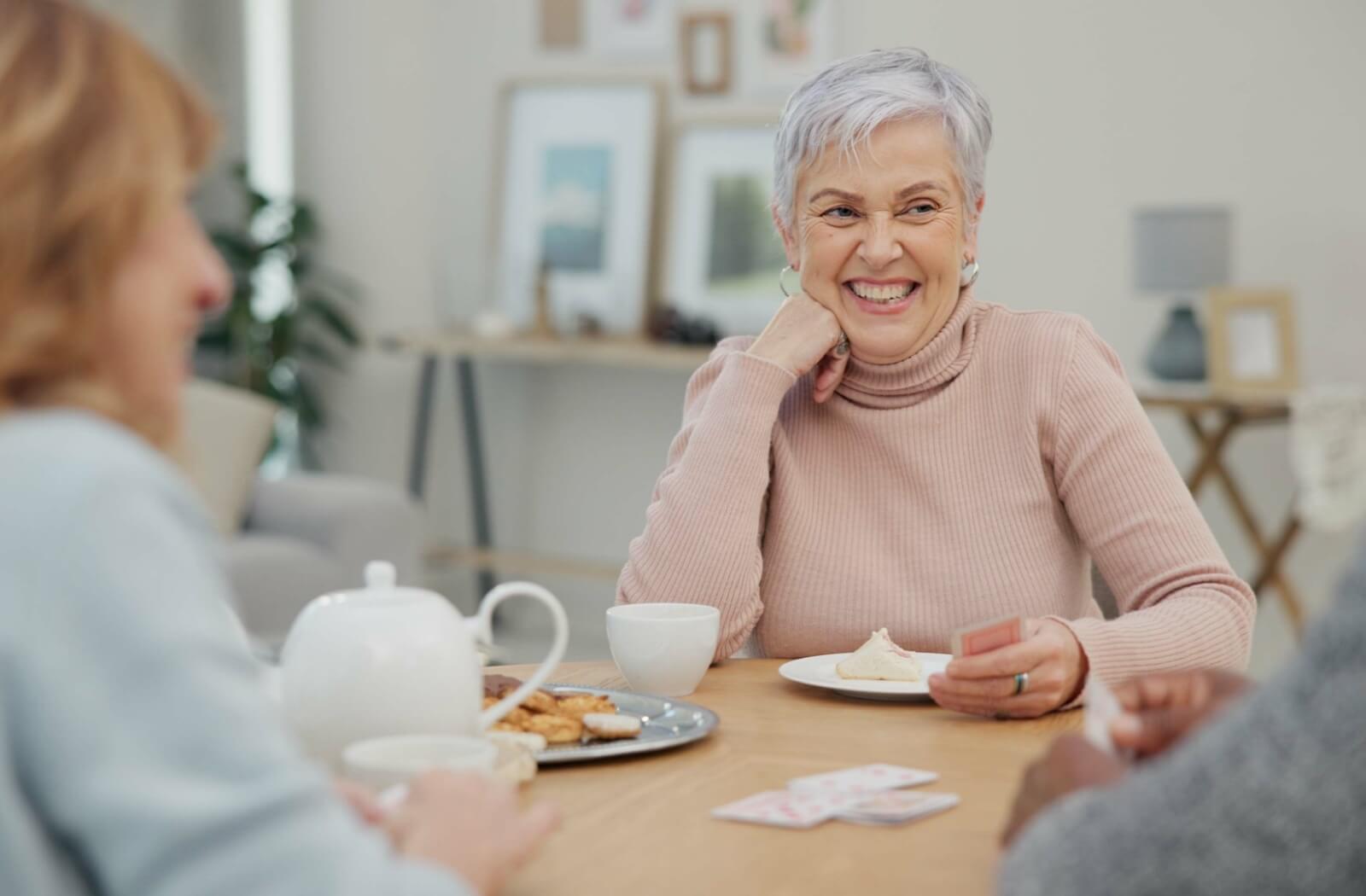 3 older adults smiling as they play cards and socialize in respite care.