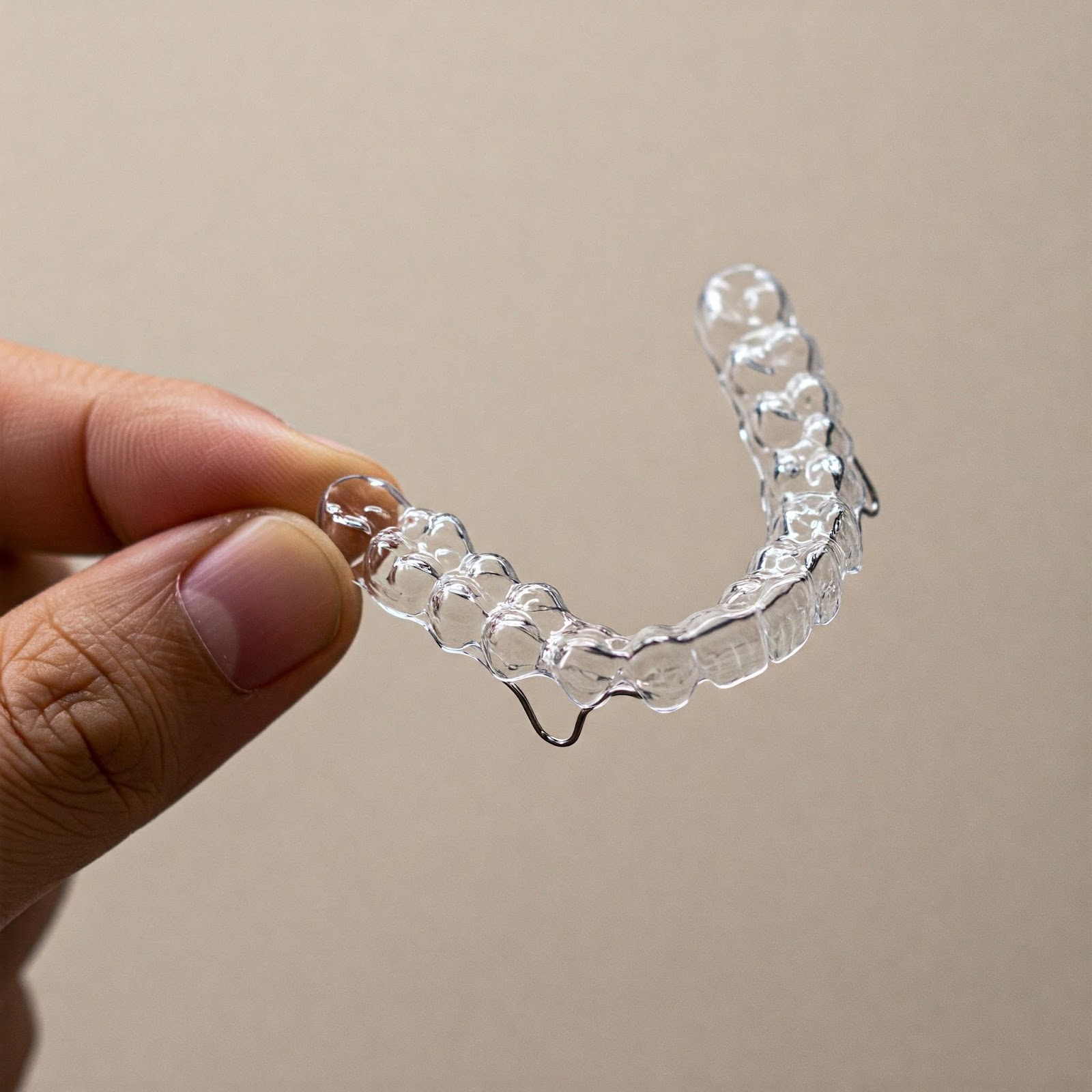 A hand holding a clear plastic dental aligner.

