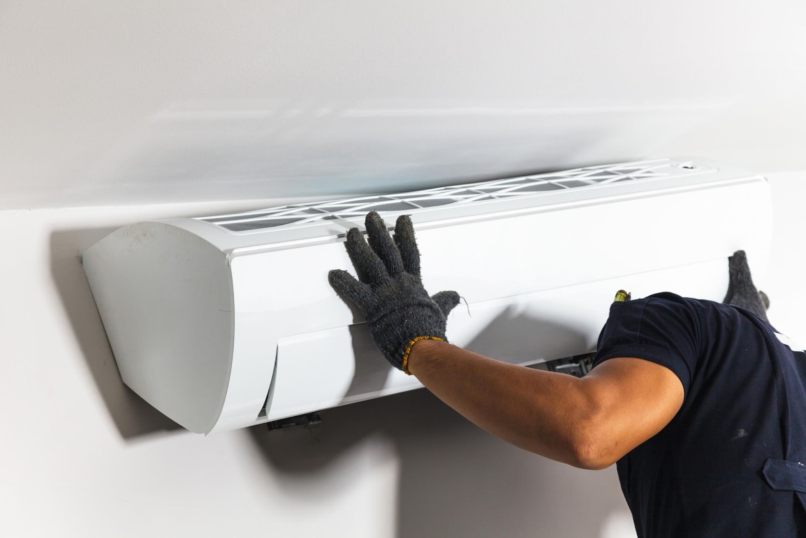 A technician in a black shirt performs air conditioning services on a unit.