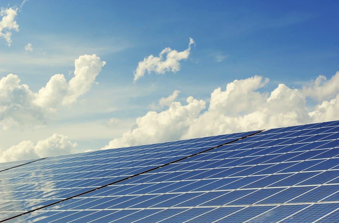 Free Sleek modern solar panels under a vibrant blue sky with clouds, symbolizing clean energy. Stock Photo