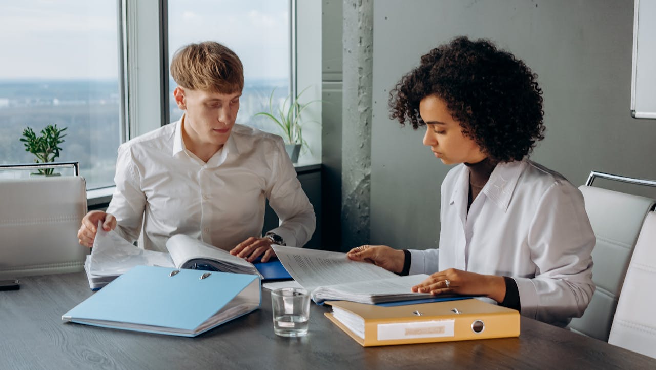 Two people engaged in discussion at a table, surrounded by papers and folders, deep in thought and collaboration.