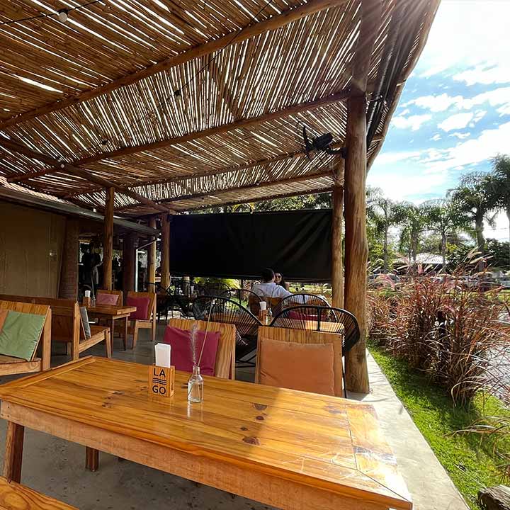 Ambiente de restaurante ao ar livre com infraestrutura de bambu, mesas de madeira e cadeiras coloridas, ideal para relaxar e apreciar uma refeição ao ar livre.