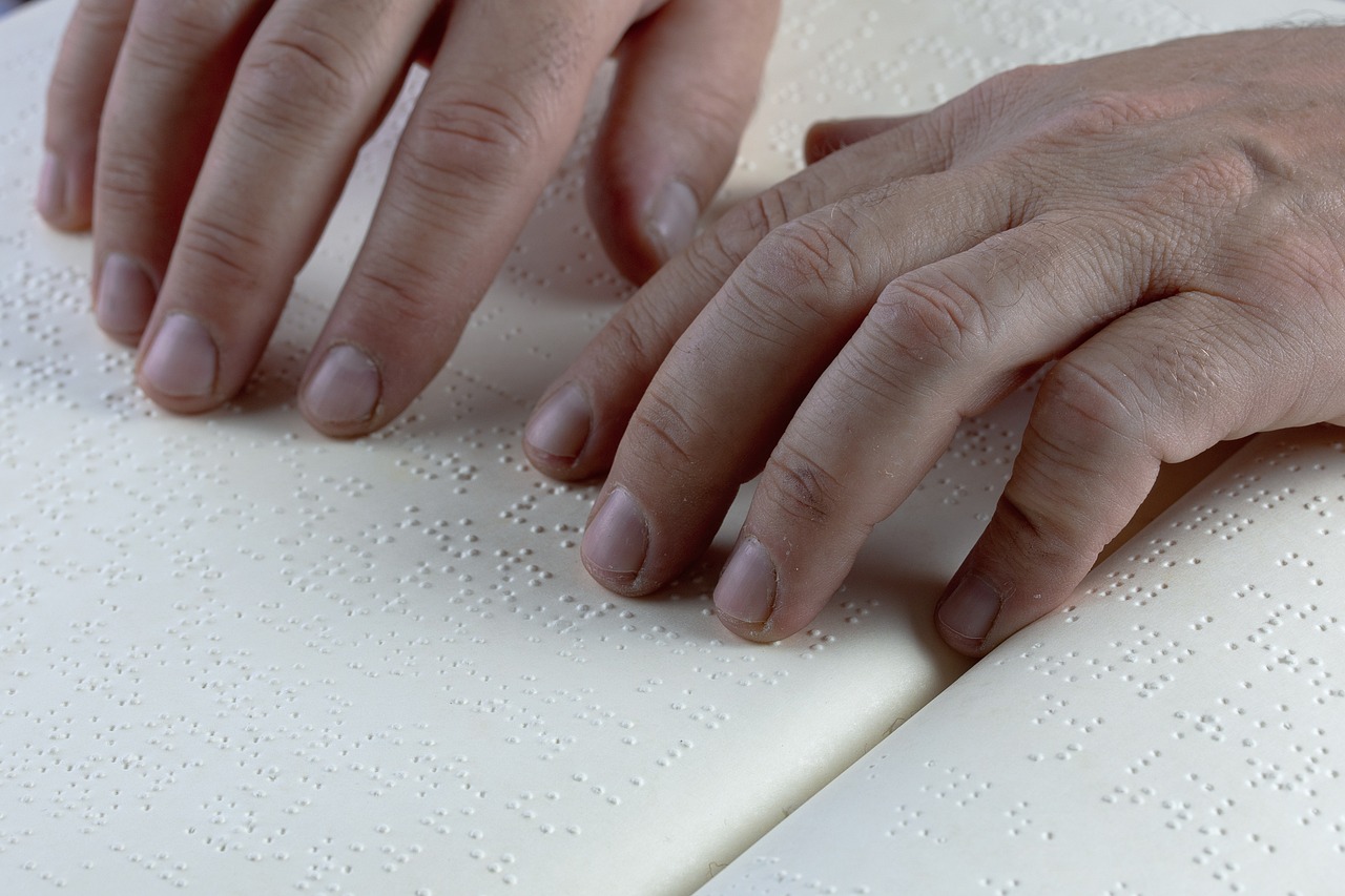 Close-up of hands reading braille text on a page, with fingers gliding across the raised dots.