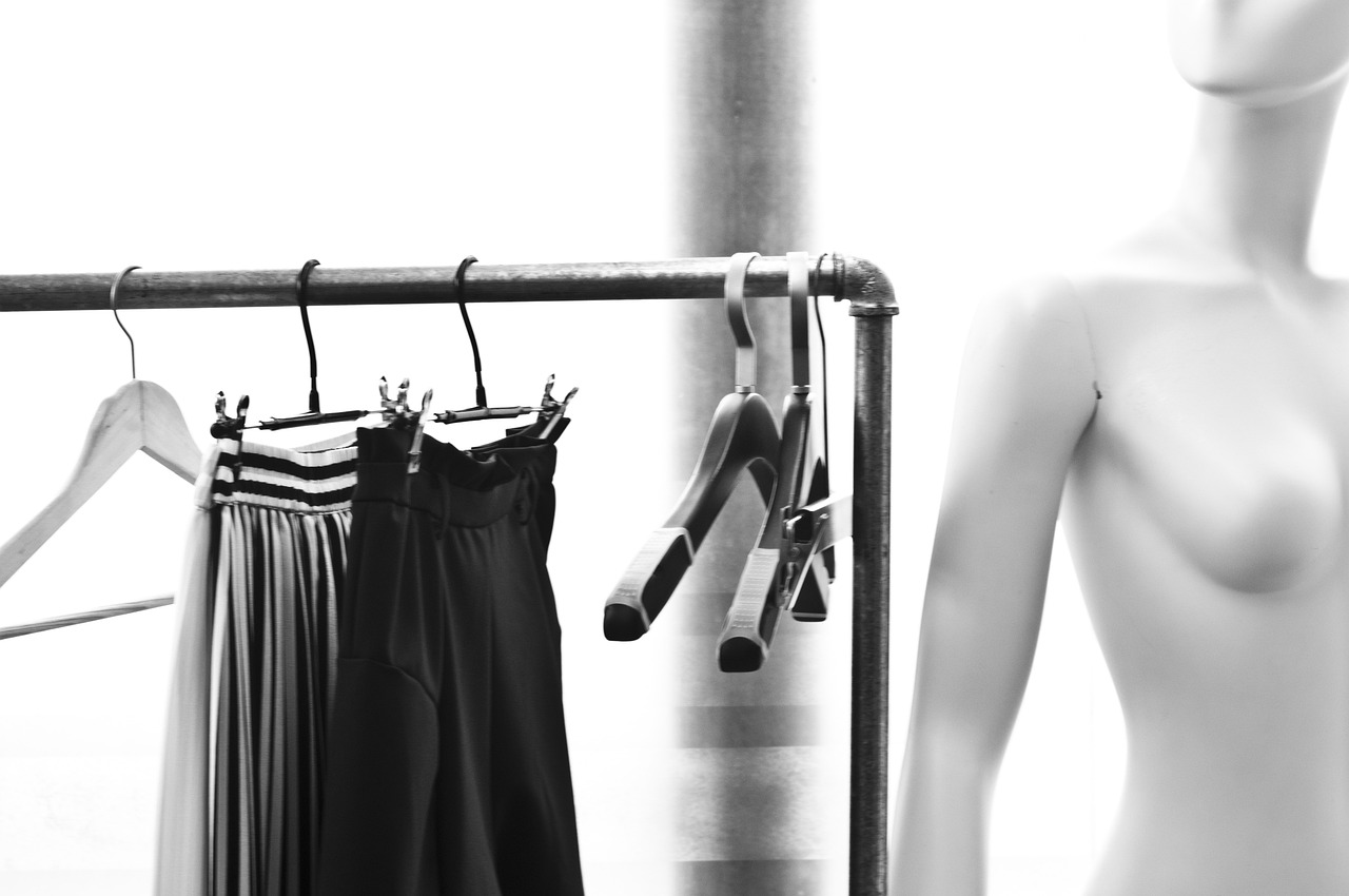 A black and white image of a mannequin with clothing hanging on a rack.  