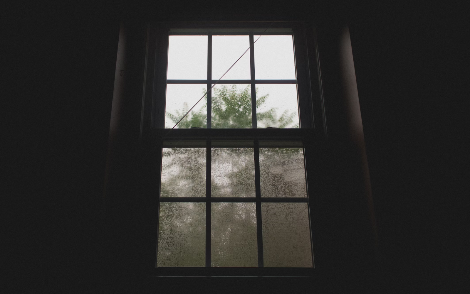 Interior view of a rain-covered window with droplets streaking down the glass.
