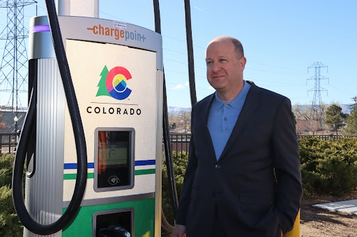 Governor Polis stands next to a ChargePoint electric vehicle charger with the Colorado State logo on it.