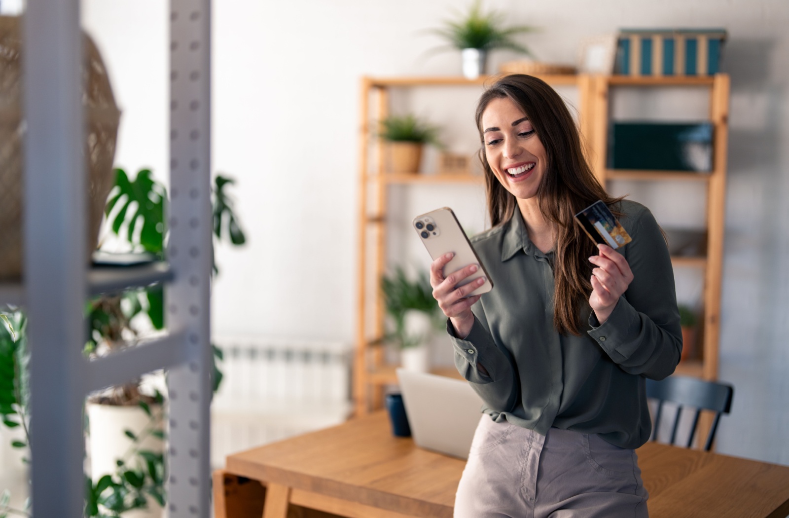 Smiling woman holding a smartphone and a credit card, making a mobile banking transaction.