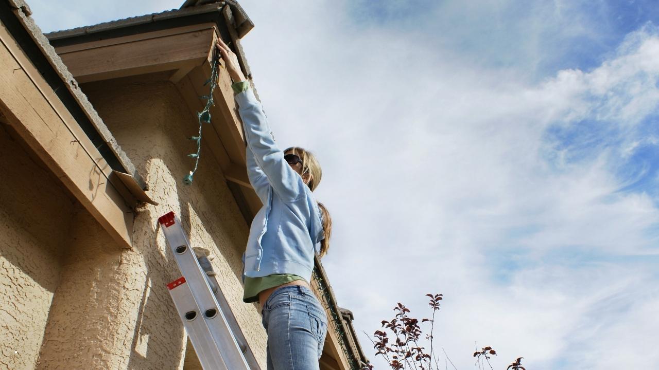 woman on ladder installing her permanent christmas lights