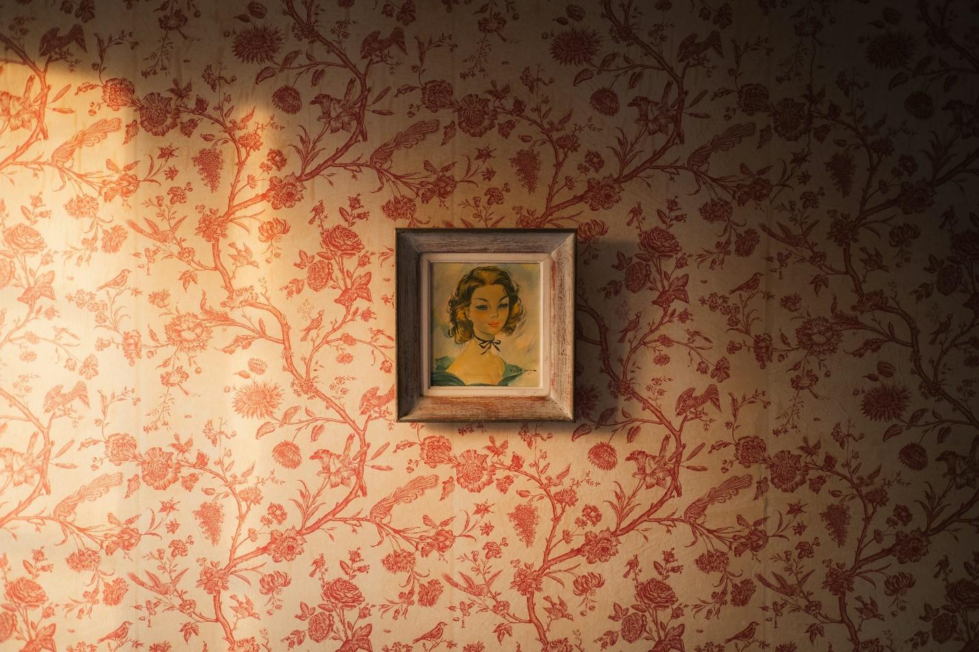 A portrait hangs on the floral wallpapered wall.