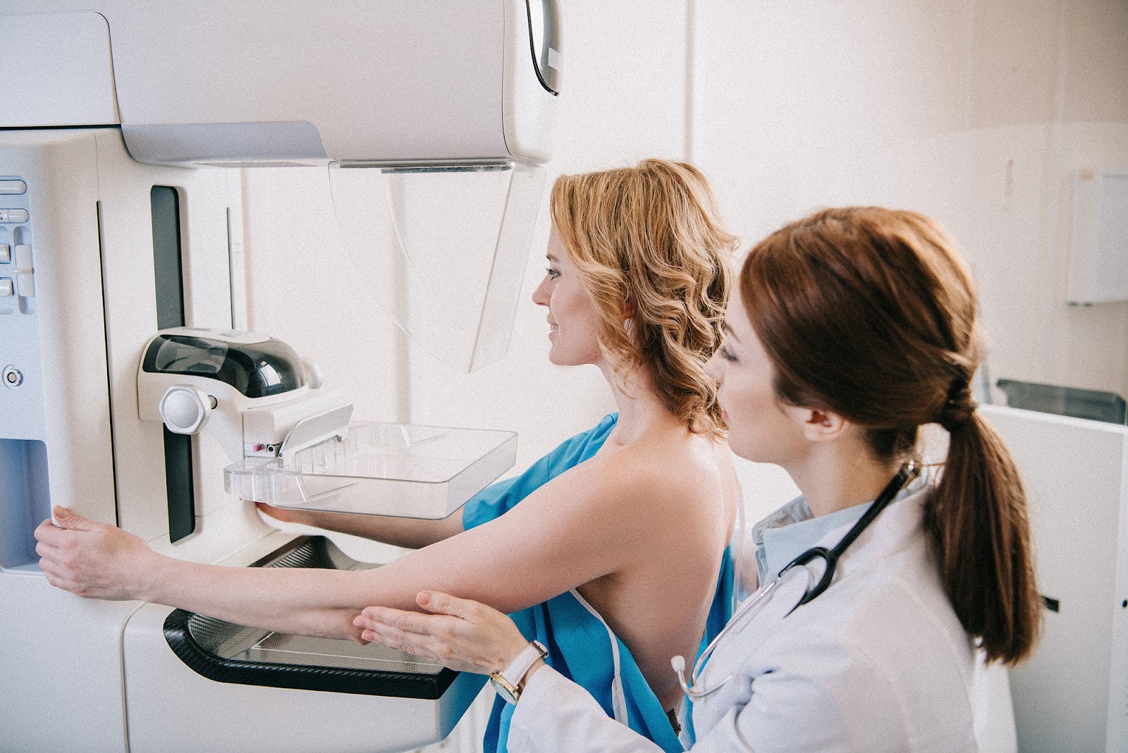 A young female patient standing with a healthcare professional while having a mammogram performed. 