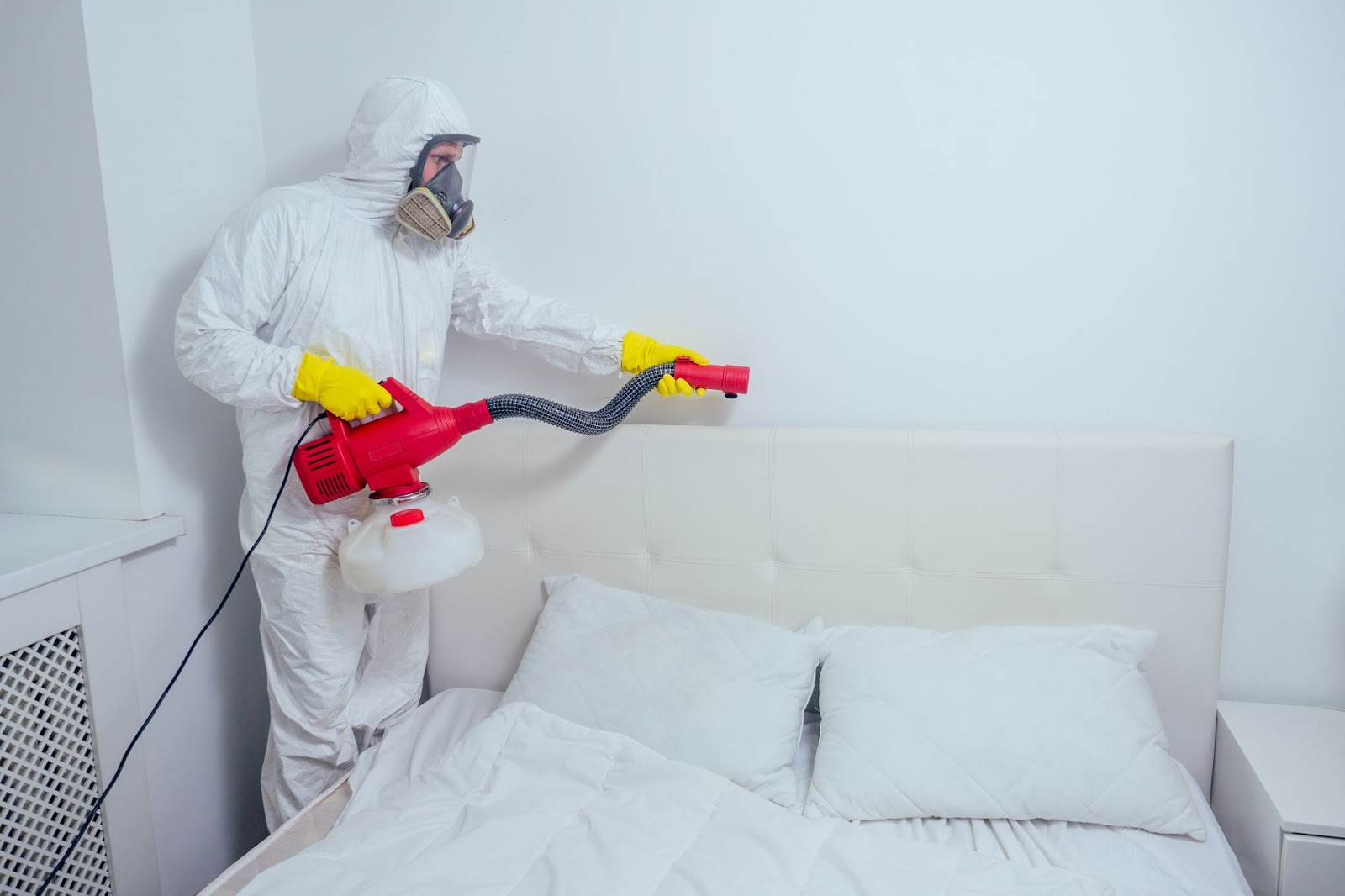 A pest control worker in protective gear treating a headboard for bed bugs.