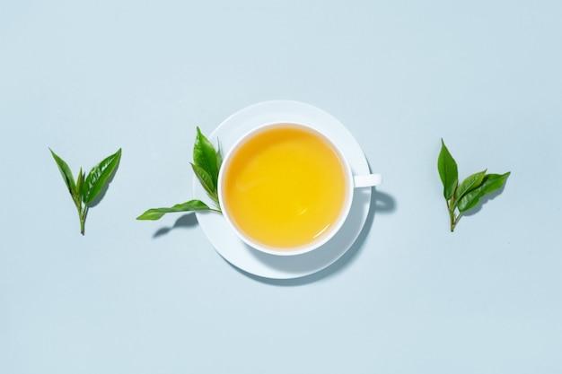 green tea brewed in cup with tea leaves on blue pastel background. top view.