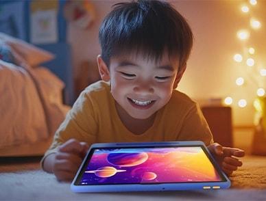 A smiling child lying on the floor, using a Lenovo Tab to view a vibrant space-themed animation in a cozy, softly lit room.