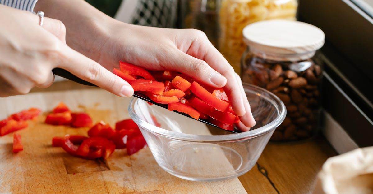 Hands slicing red bell peppers on a cutting board with fresh ingredients nearby.