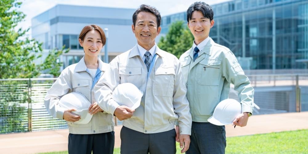 作業服を着た3人の技術者チームが屋外で並んで微笑む様子、安心と信頼を感じさせるイメージ