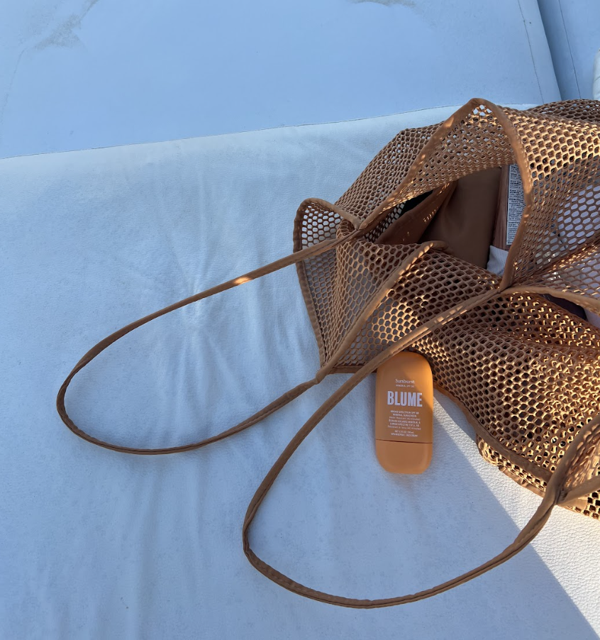 Blume sunscreen bottle in a brown mesh beach bag on a light blue poolside lounge chair in natural sunlight