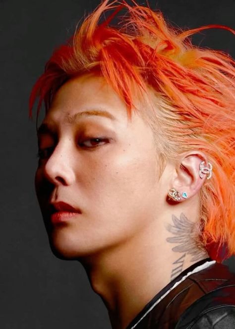 This contain BIGBANG's G-Dragon   with bright orange hair and piercings on her ears is looking off to the side