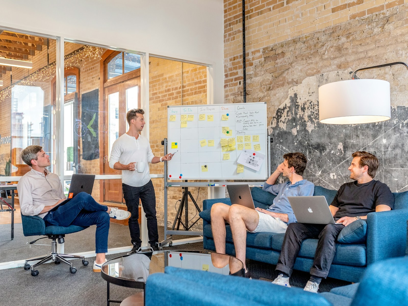 A diverse group of people gathered around a table, brainstorming ideas with a whiteboard in the front.