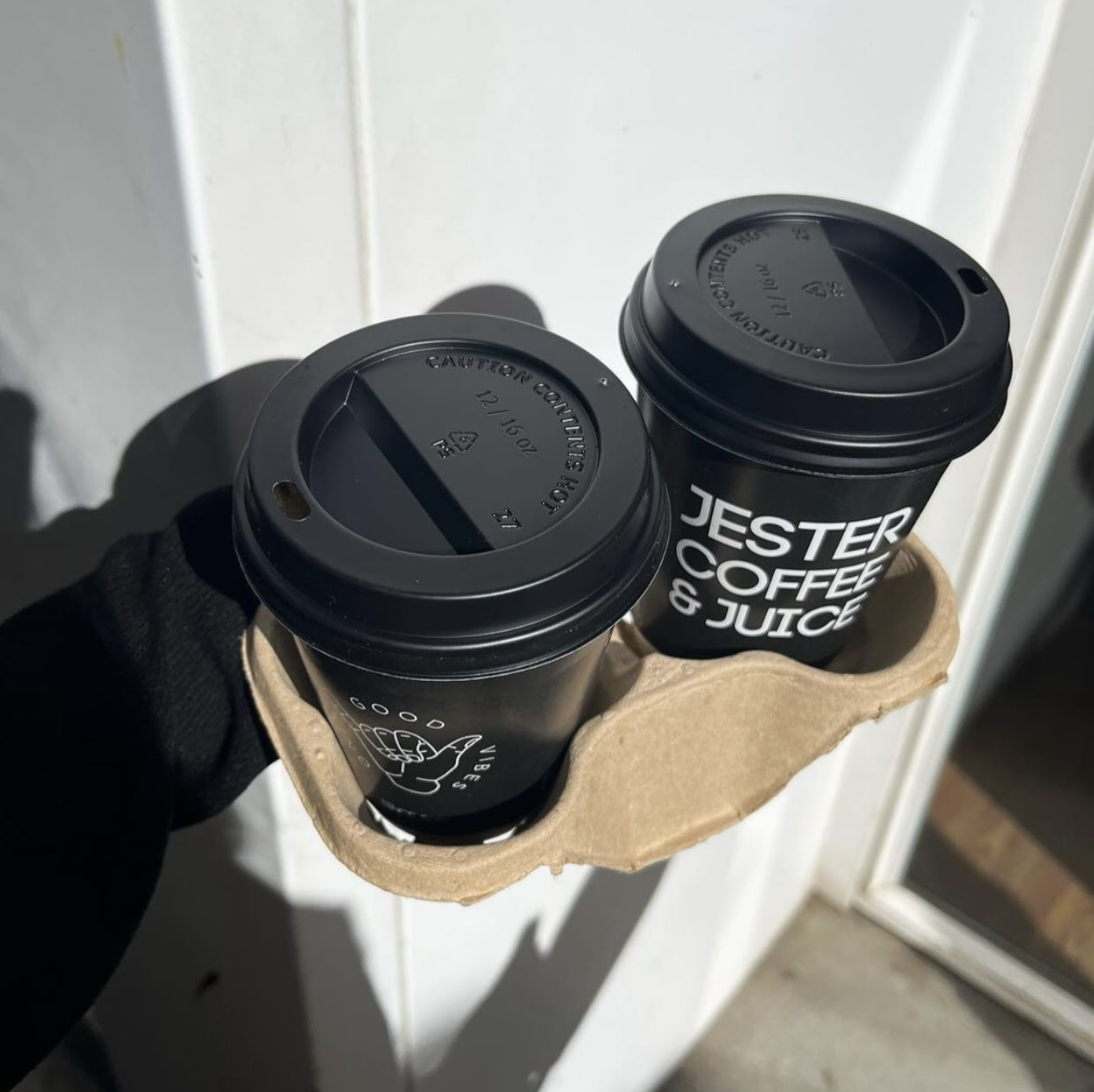 Two black paper cups with lids placed on a cardboard cup holder.