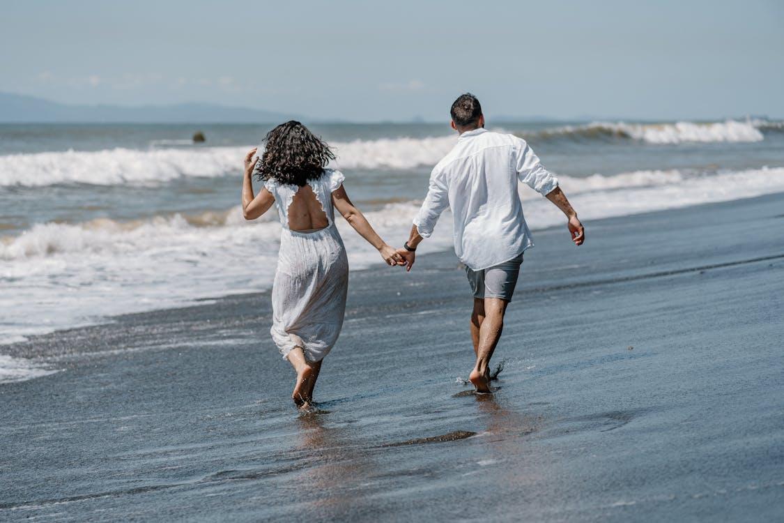 Free Couple Holding Hands on a Sandy Beach Stock Photo, honeymoon itinerary
