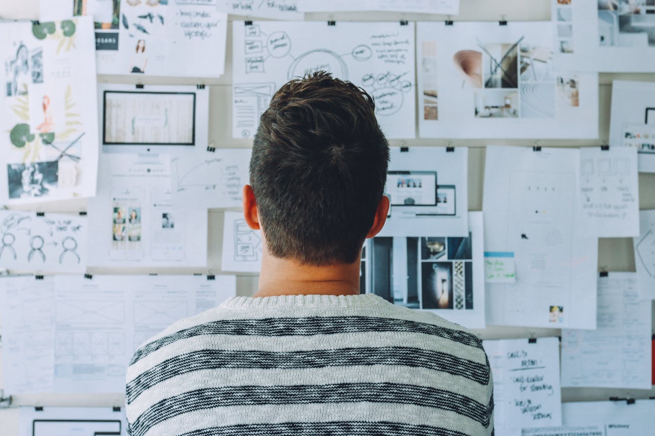 A man examines a wall filled with papers, lost in thought as he studies the information displayed before him.