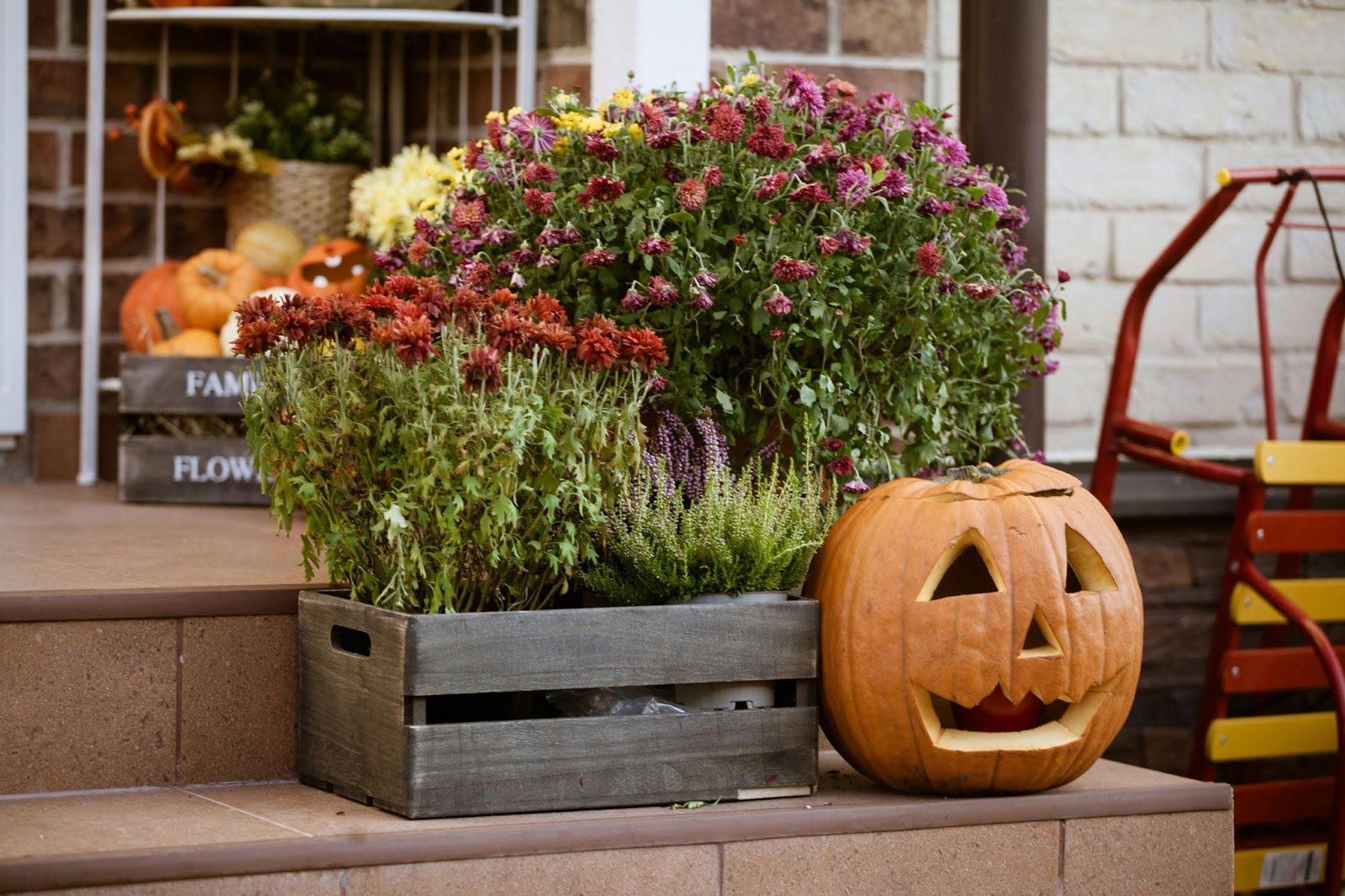 Front porch with a single carved pumpkin and two wooden boxes filled with fall florals and decorative gourds