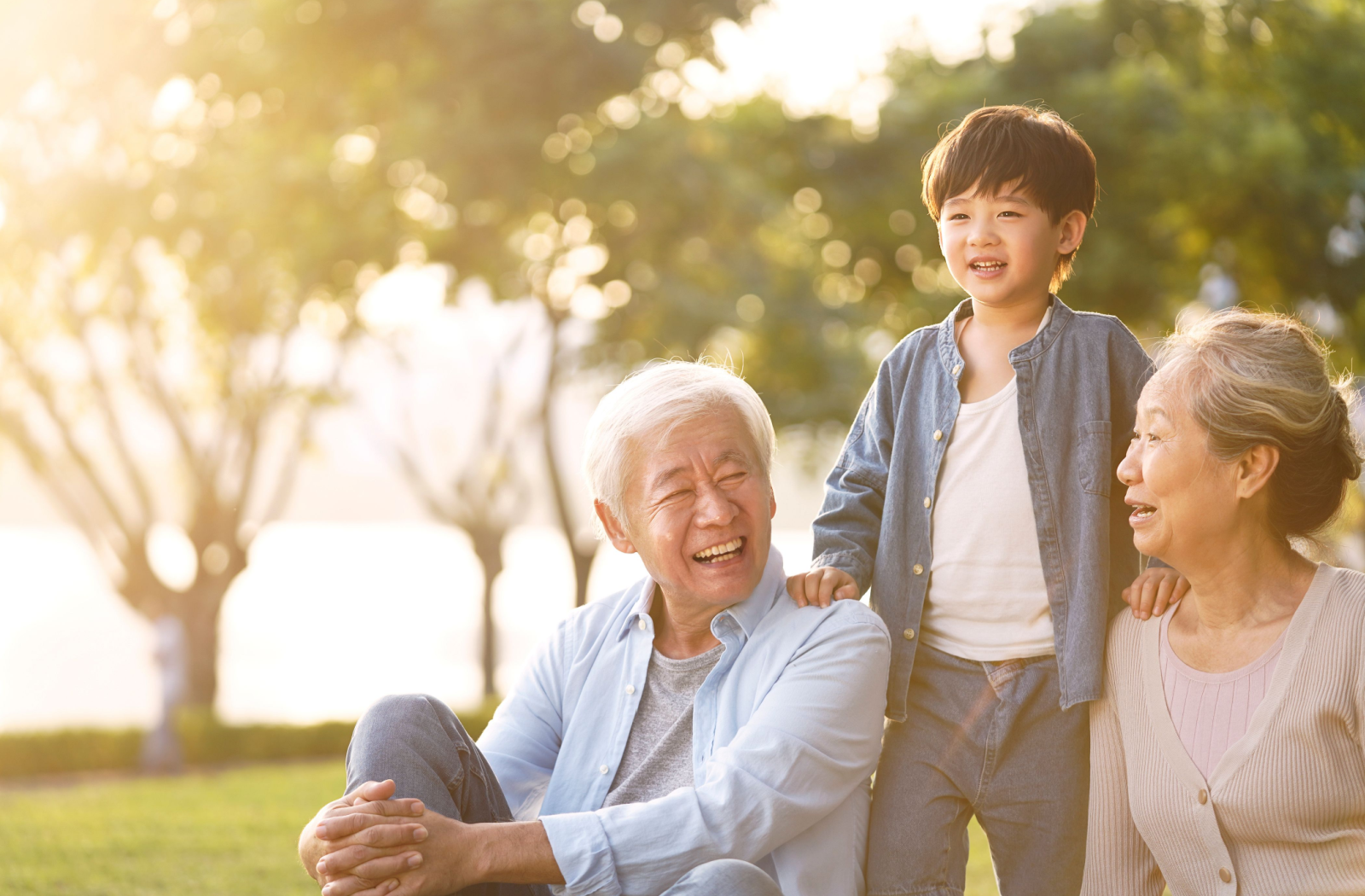 Grandparents sitting in the park and laughing with their young grandchild.