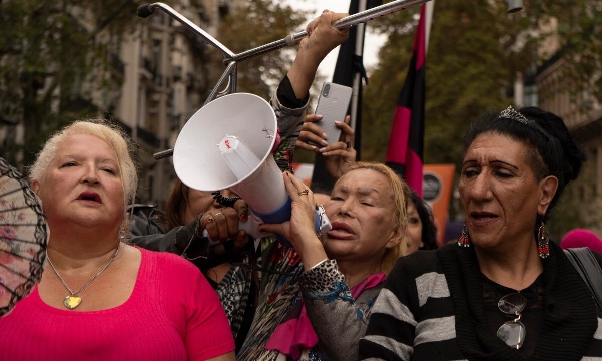 3 people at demonstration. Person in middle holding megaphone.