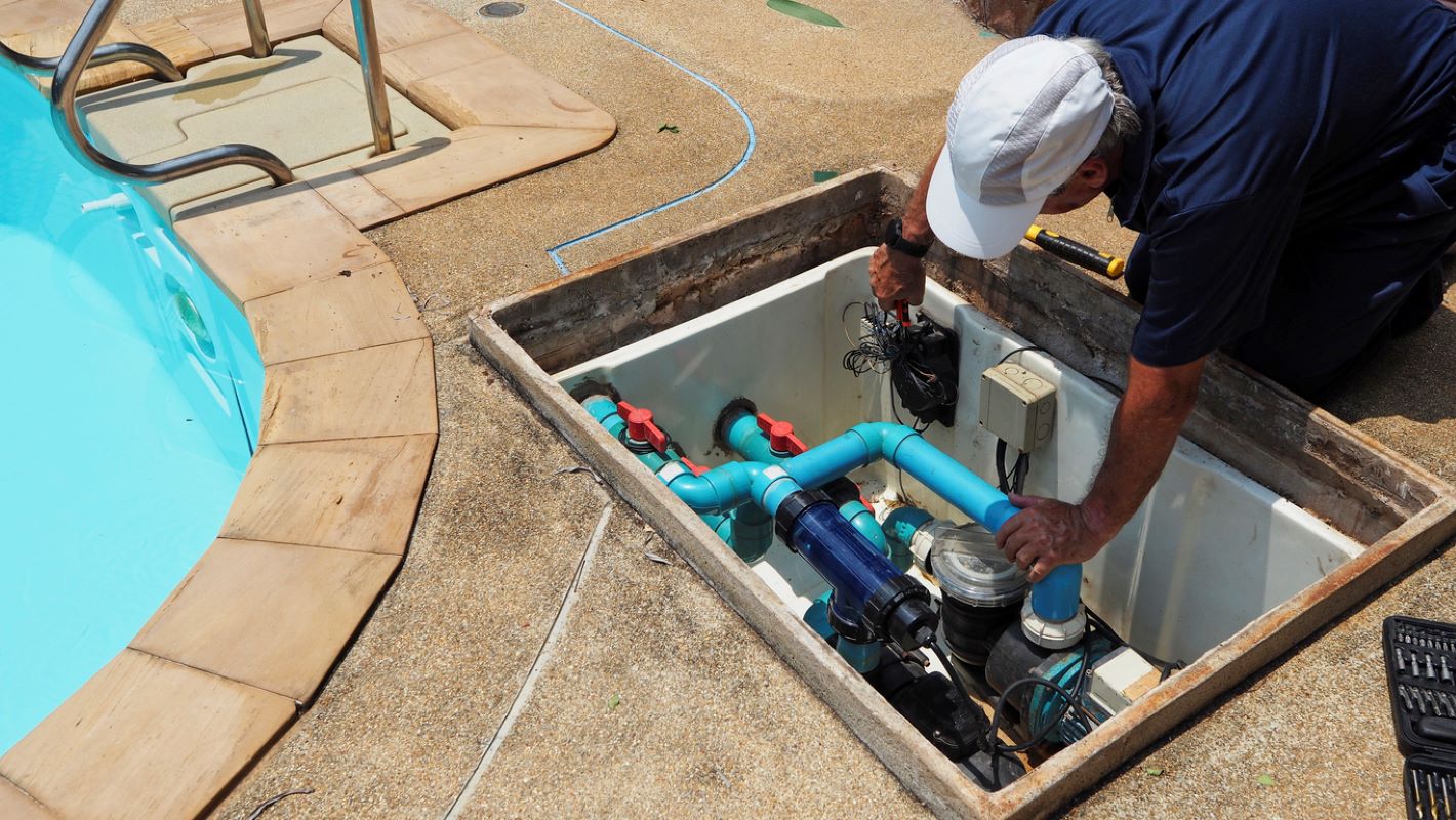 A pool care technician performs maintenance on a swimming pool water pump.