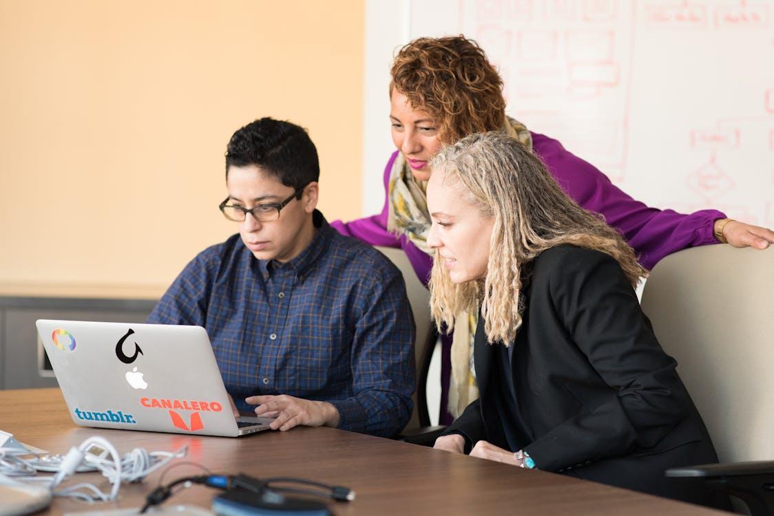 Free Team of three people collaborating on a laptop in an office setting. Stock Photo